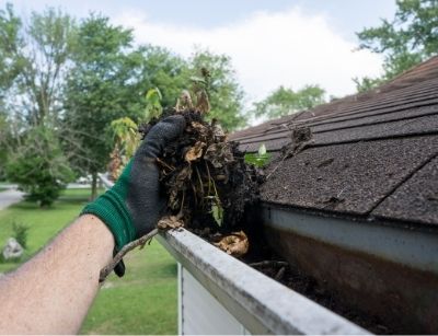 Person removing dirt and debris from gutter