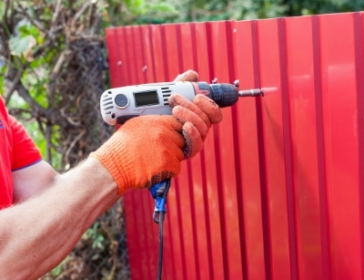 Person drilling into a red metal fence